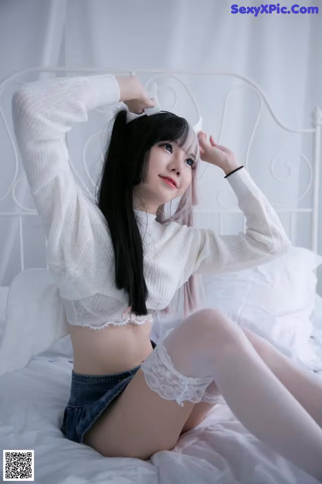 A woman sitting on top of a bed wearing a white sweater.