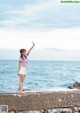 A woman standing on a wall near the ocean.