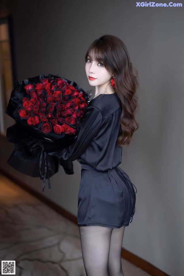 A woman in a black dress holding a bouquet of red roses.