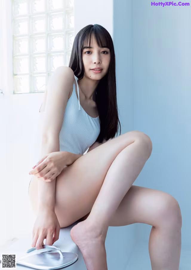 A woman sitting on top of a white table next to a window.