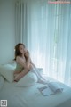 A woman sitting on a bed with a book and glasses.