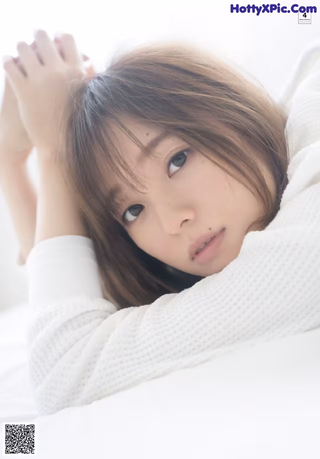 A young woman laying on a bed with her hands on her head.