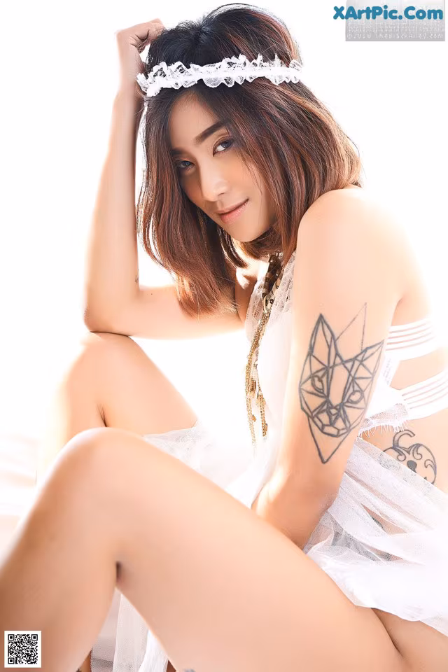 A woman with a tattoo on her arm sitting on a bed.