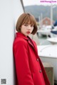 A woman in a red coat leaning against a wall.