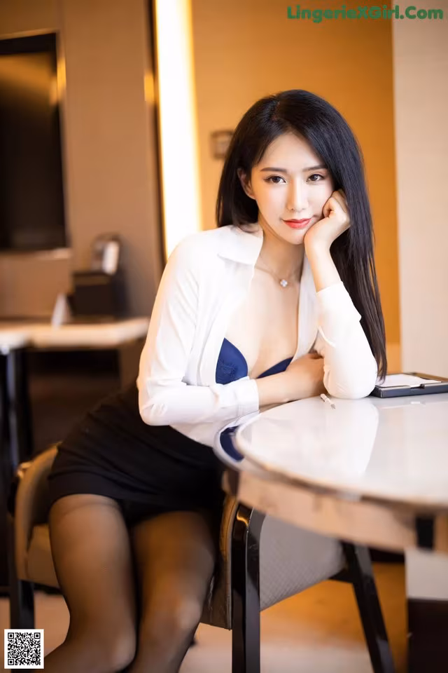 A woman sitting at a table with her hand on her chin.