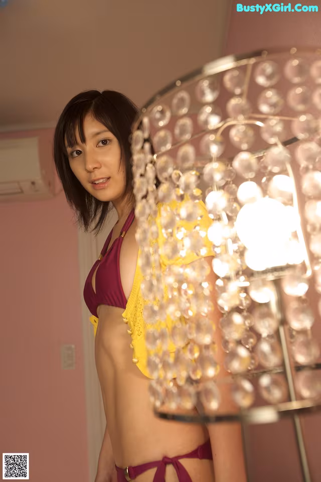 A woman in a yellow bikini standing next to a lamp.