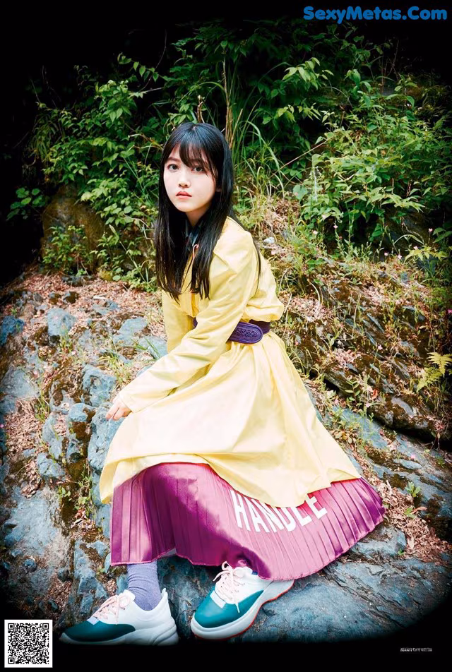 A woman in a yellow dress sitting on a rock.