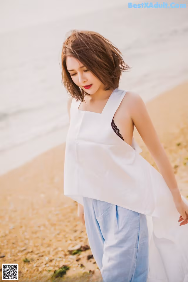 A woman in a white top and blue pants on the beach.