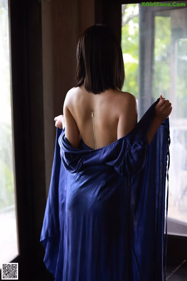 A woman in a blue dress standing by a window.
