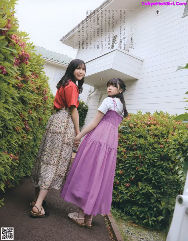 Two young women standing next to each other in front of a house.
