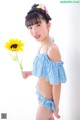 A young girl in a blue and white bikini holding a sunflower.