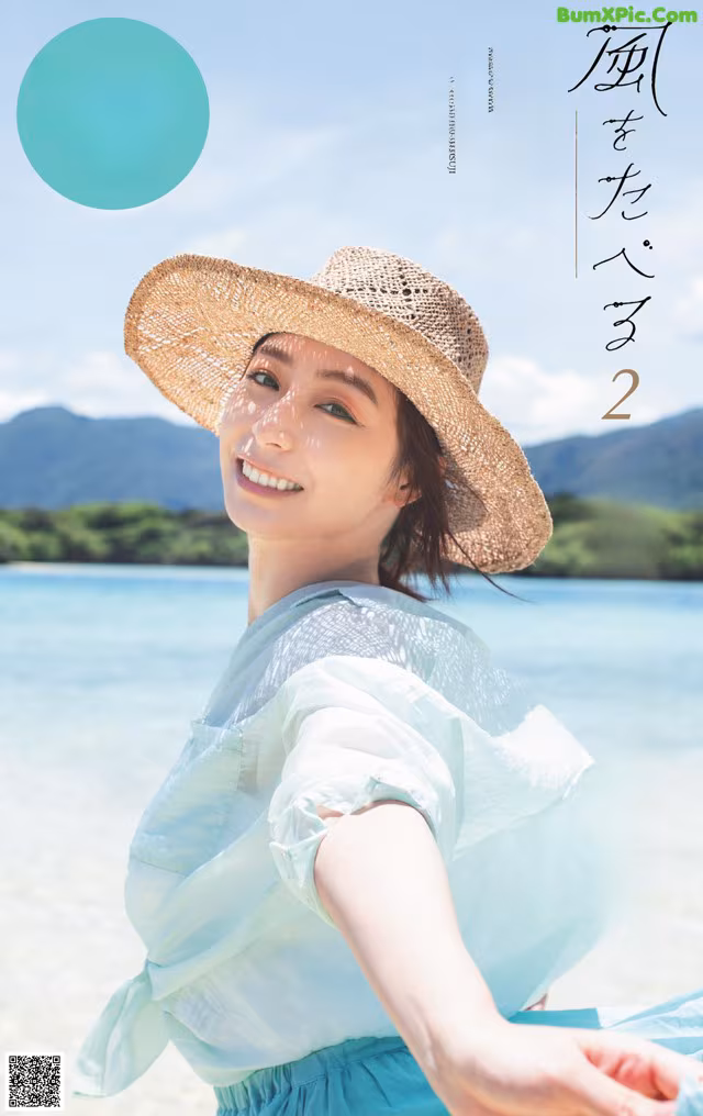 A woman in a straw hat sitting on a beach.