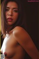 A naked asian woman posing in front of a black background.