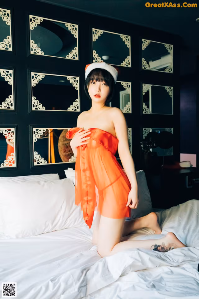 A woman in an orange dress sitting on a bed.