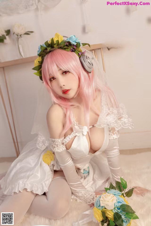 A woman with pink hair wearing a white dress and a flower crown.