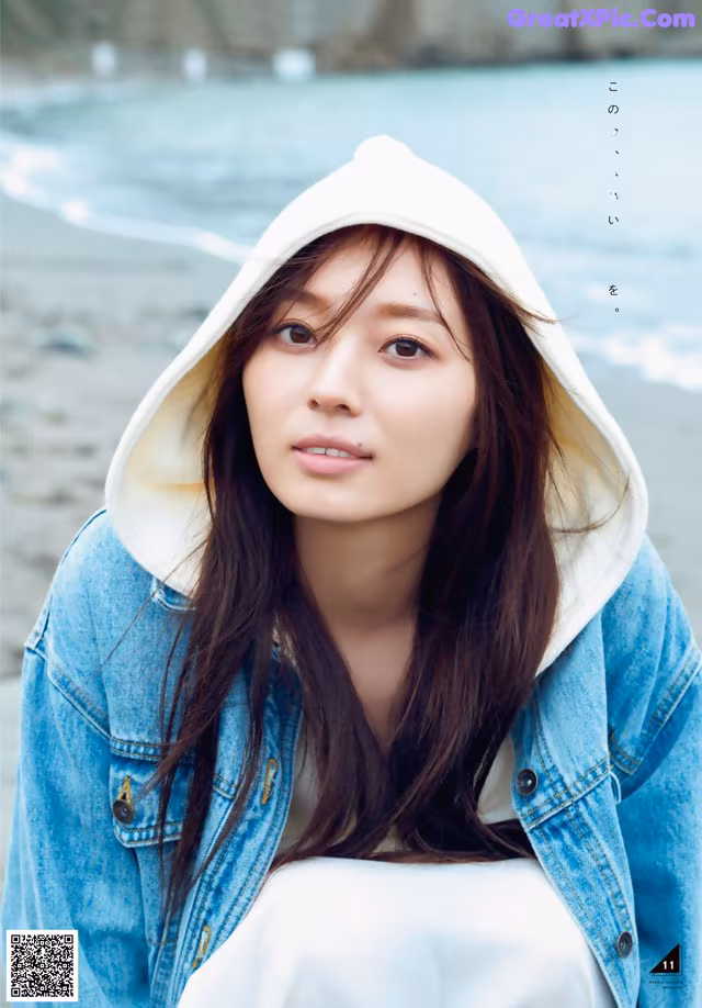 A woman wearing a white hoodie sitting on a beach.